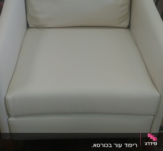 כורסה מרופדת בצבע קרם על רצפת עץ